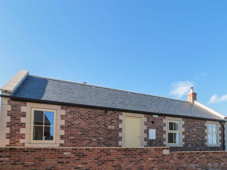 A brick building with three windows and a door behind a brick wall at Glebe Cottage in Embleton