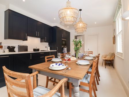 A kitchen with dark cabinets and a wooden dining table set with plates and glasses at Collett House Southwold