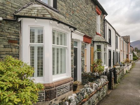 A row of stone and brick houses with small front gardens along a sidewalk at Derwent Cottage in Keswick