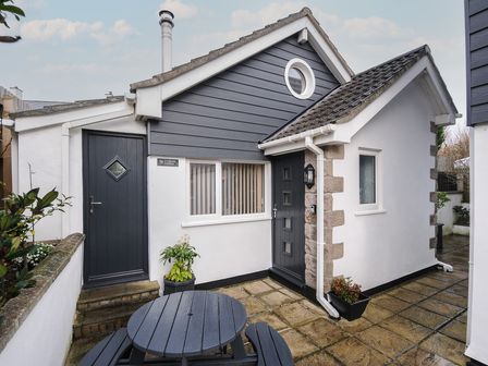 The exterior of a small house with a round table and benches on a stone patio at Curlew Lodge in Newquay