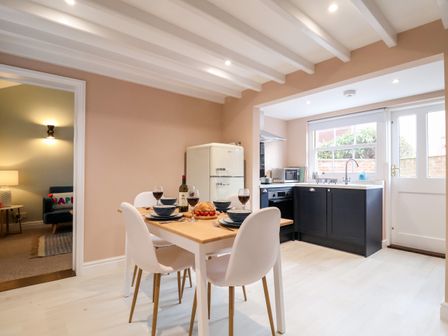 A kitchen with dining table set for four near a refrigerator and window at Poppy Cottage in Southwold