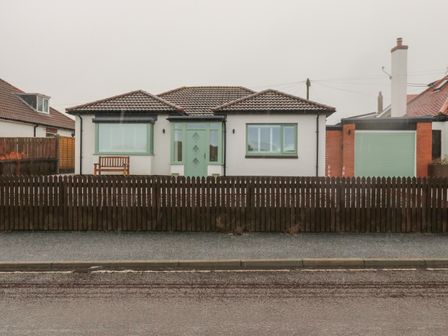 A house with a green door, two windows, a wooden bench, and a wooden fence at Bamburgh Dunes Bamburgh near Seahouses