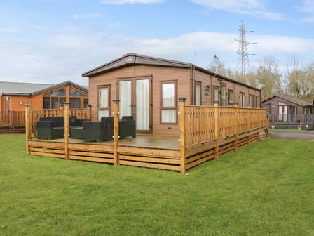 A wooden cabin with a fenced deck and outdoor furniture on grass at Hudson's Hideaway in South Lakeland Leisure Village