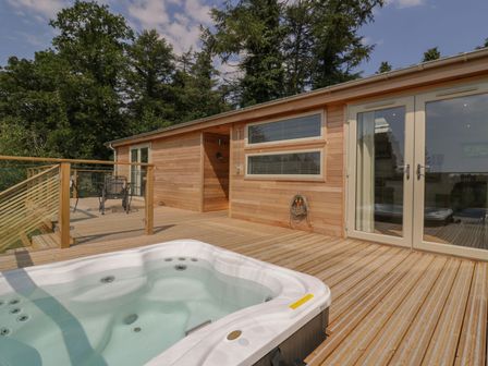 A wooden deck with a hot tub a table and chairs outside a building with glass doors and trees in the background at 2 Faraway Fields in Dobwalls