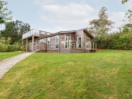 A wooden house with glass railings and a gravel path on a grassy hill surrounded by trees at 1 Southern Place in Dobwalls