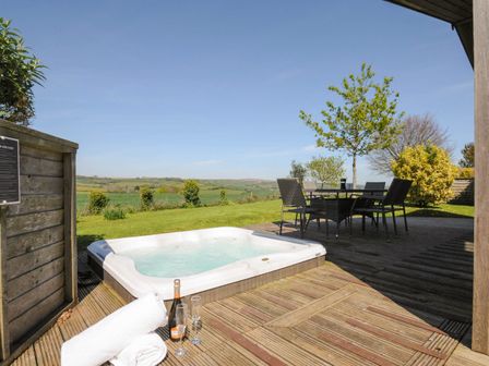 An outdoor deck with a hot tub table with chairs towels a bottle and glasses overlooking fields at 4 Horizon View in Dobwalls