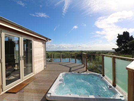 An outdoor deck with a hot tub and glass railing overlooking a body of water at 14 Faraway Fields in Dobwalls