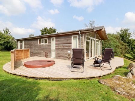 A wooden cabin with large windows and two black chairs on a wooden deck in a grassy area at 11 Horizon View in Dobwalls
