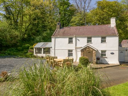 A white two-story house with a patio table and chairs in front at Mill House Main House in Sarn Meyllteyrn
