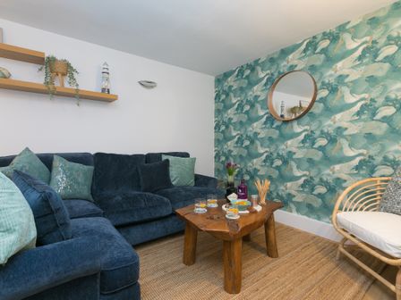 A living room with a blue sofa wooden coffee table and a patterned wall with a round mirror at Dream Achieved in St Ives