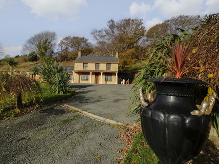 A driveway with plants and a black planter leading to a two-story house surrounded by trees at Bryn Berthen in Penrhyndeudraeth