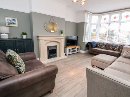 A living room with sofas a fireplace a television and a bay window at Tan Y Fron in Penrhyn Bay