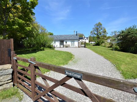 A gravel driveway leading to a white cottage with a wooden gate labeled Brook Cottage in Llangoed near Beaumaris