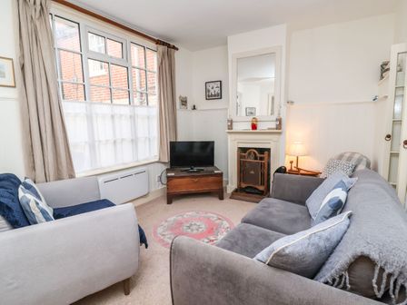 A living room with two sofas a television on a wooden stand a fireplace and a window with curtains at Tuckaway Cottage in Aldeburgh
