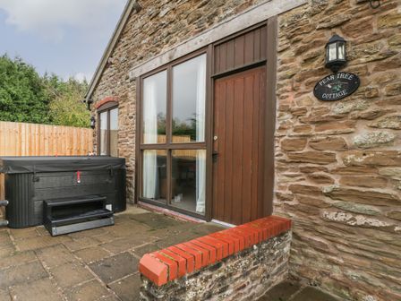 Exterior of a stone cottage with wooden door and window and a covered hot tub on a paved patio at Peartree Cottage Stanford Bishop near Bromyard