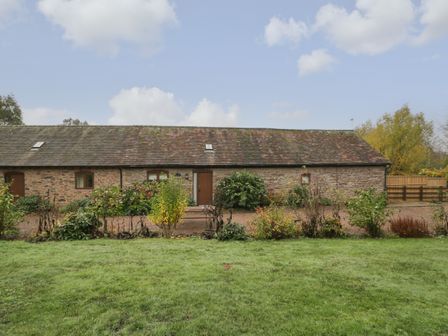 A stone building with a wooden door and windows surrounded by shrubs and grass at Clover Patch Cottage in Stanford Bishop near Bromyard
