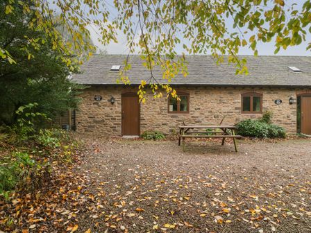A stone cottage with two brown doors and two windows with a wooden picnic table in front of it at Honeysuckle Cottage Stanford Bishop near Bromyard