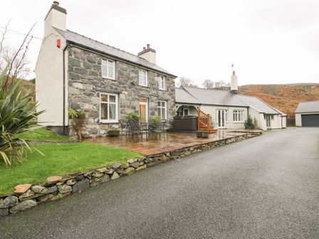 A stone and white exterior house with outdoor table and chairs on a patio with a driveway and garage at Lakeside Cottage in Llanrug