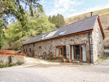 A stone house with large windows and potted plants surrounded by trees and hills at Ysgubor Craig Y Gronfa in Mallwyd