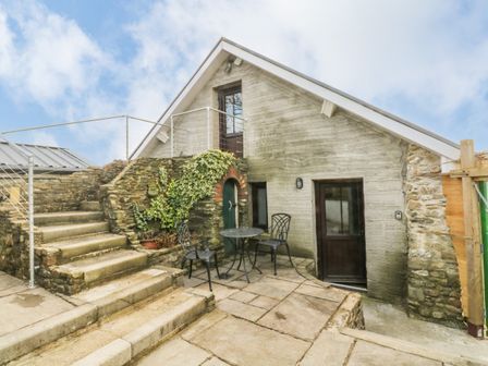 Exterior view of a stone and concrete house with stairs potted plants and a small table with two chairs at Green Grove Barn in Peniel near Carmarthen