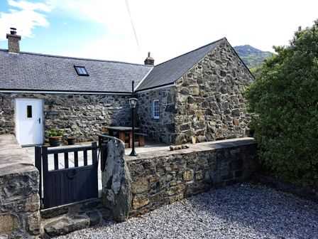 Stone house with slate roof and white door courtyard with wooden picnic table and black gate Llain Fadarn Dinas near Nefyn