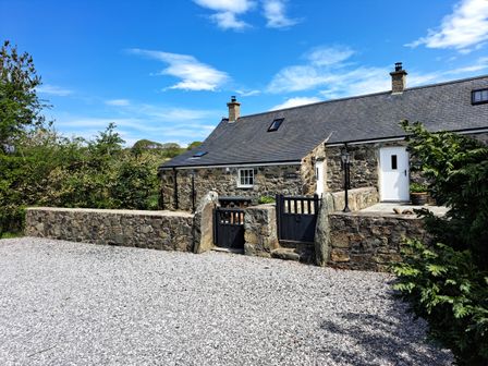 A stone house with black wooden gates and a gravel driveway at Tir Eironwy in Dinas near Nefyn