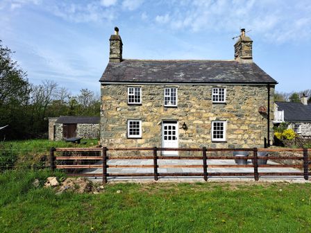 A stone house with six windows and a white door with a fenced patio and green grass at Ty Bwlcyn in Dinas near Nefyn