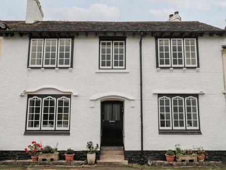 Front view of a white two story house with black framed windows and a black door with potted plants outside at The Pound in Porlock