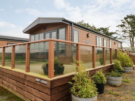 An exterior view of a wooden lodge with glass railing and potted plants outside at Reef Retreat in Broad Haven