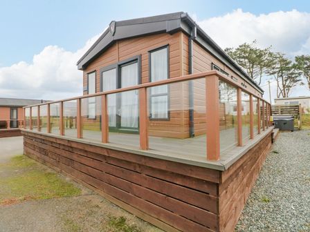 A wooden cabin with glass railing on a deck surrounded by gravel and grass at Seahorse Retreat in Little Haven near Broad Haven