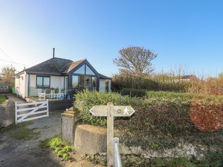 A detached house with a patio and outdoor dining furniture next to a hedge and a pedestrian signpost at Haulfryn in Moelfre
