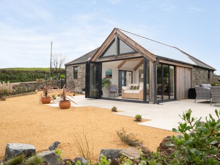 A modern stone house with glass folding doors open to a seating area with sofa and chair at The Rum House in Porthallow