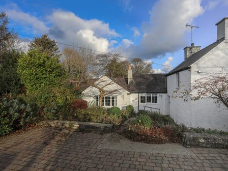 A white building with windows surrounded by trees and bushes under a blue sky at Ty'n Lon in Moelfre