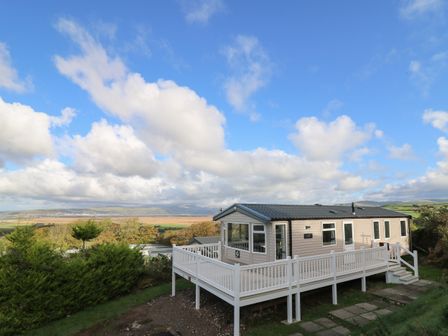 A mobile home with a white deck overlooking a green landscape and hills at Gwent 74 in Borth