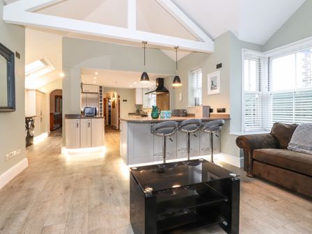 An open kitchen and living area with a kitchen island and stools a brown sofa and black coffee table at Blencathra in Keswick