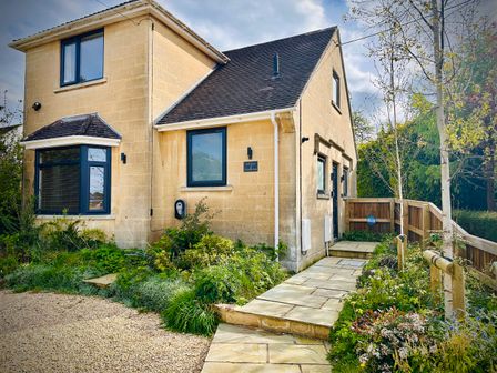 A stone house with blue window frames a pathway and garden at Birch House in Corsham