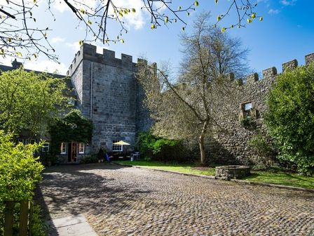 A courtyard with cobblestone ground surrounded by stone walls and a tower with trees and shrubs at Craster Tower Penthouse in Craster