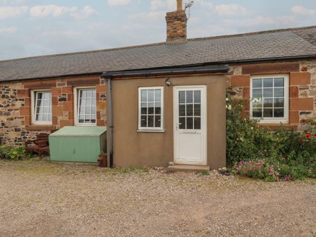 A stone cottage with a white door and windows a green storage box and flowers at No2 Budle Bay Cottage in Bamburgh