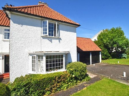 A white two-story house with a tiled roof and large windows with bushes in front at Inveray in Seahouses