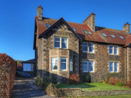 A stone house with multiple windows a gravel driveway and a grassy front yard at The Villas No3 Embleton