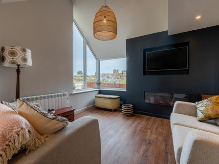 A living room with two sofas wooden floor a floor lamp wall-mounted television and a window with a view at Castle View Bamburgh
