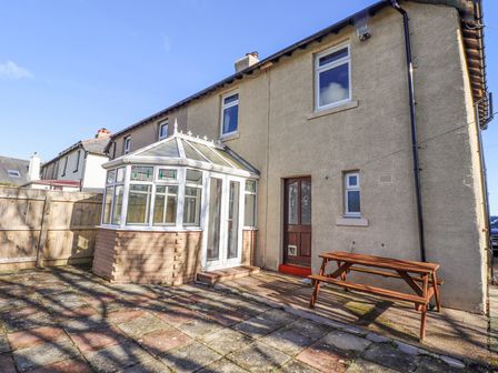 An outdoor patio area with a conservatory attached to a house and a wooden picnic table at St Marys Cottages No1 in Low Newton-by-the-Sea
