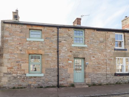 Stone exterior of a house with green door and windows at Hares Form in Seahouses