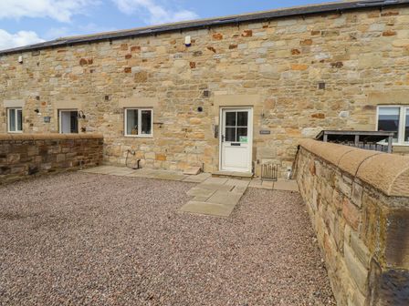 An enclosed stone courtyard with a white door and windows on a stone building at The Mustard Pot in Acklington