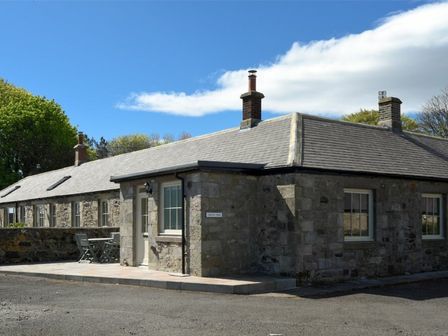 Stone building with multiple chimneys and outdoor seating area at Castle View Glororum in Bamburgh