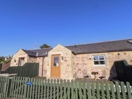 A cottage with a fenced garden and seating area at Dunlin Cottage - Lucker Steadings Lucker