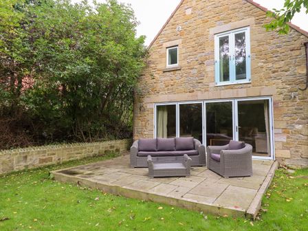 An outdoor patio with wicker furniture including a sofa armchair and coffee table outside a stone house at Quarry Haven in Bamburgh