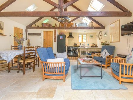 An open plan living area with blue cushioned wooden chairs a coffee table a dining table with chairs and a kitchen area with appliances at The Byre at Warkworth