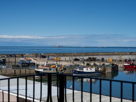 A harbor with fishing boats docked and a calm sea in the background at Lobster Lodge in Seahouses
