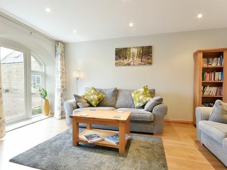 A living room with a gray sofa two patterned cushions a wooden coffee table bookshelves and a large window at East Havers in Alnwick